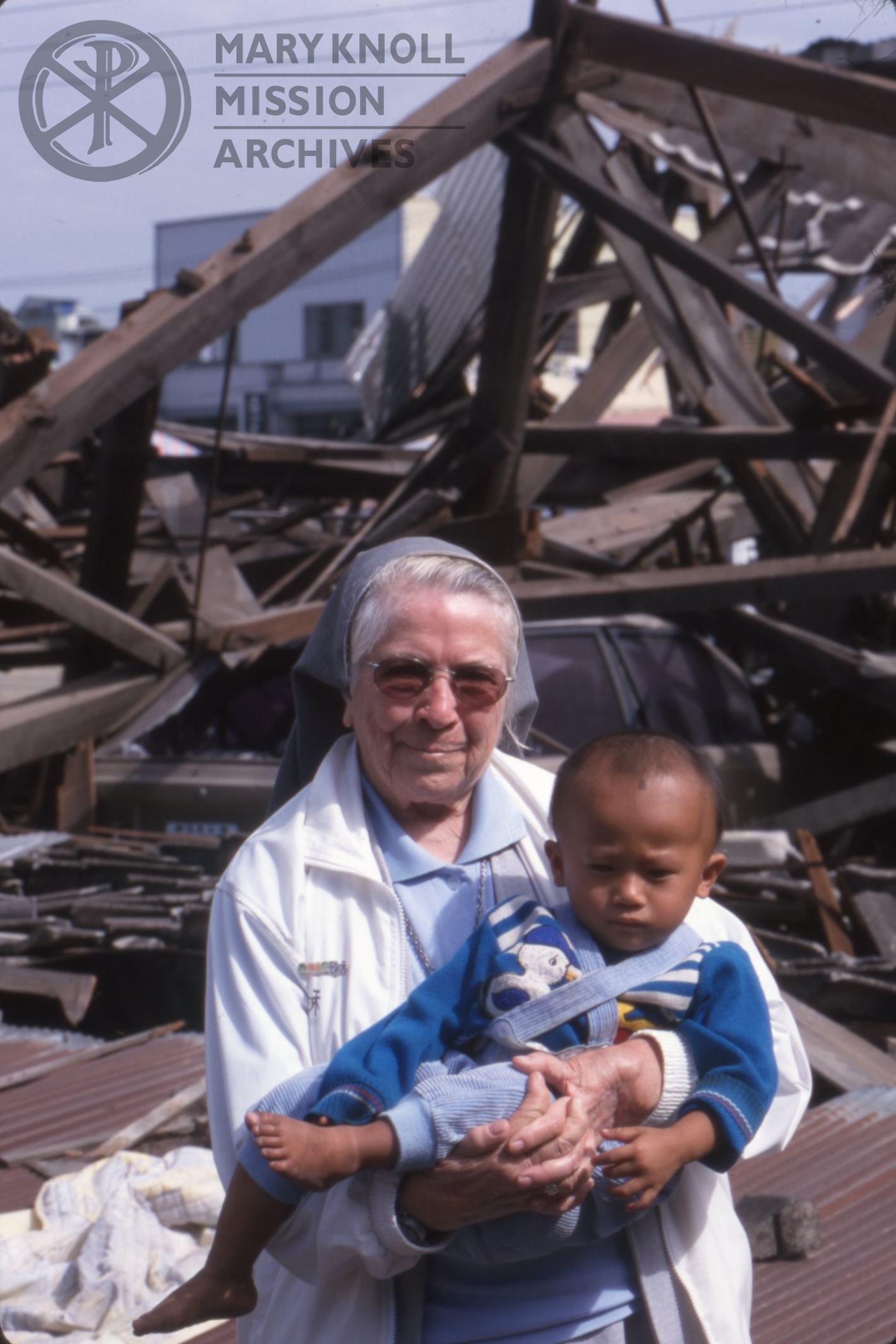 Sr. Paulita Holding a child in front of rubble / Photographer: S Michael Bisceglie